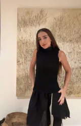 Vestido corto color beige confeccionado en lino natural, con corpiño fruncido, cuello alto con pequeño volante y falda de caída irregular con aplicaciones de cuero y pelo. Diseño asimétrico.