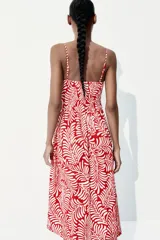 Vestido midi de breteles finos con estampado de hojas en color blanco sobre fondo rojo. El cuerpo es de punto smock, tiene escote cuadrado, costura fruncida en la cintura y falda con vuelo.