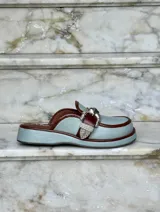 Zuecos negros de cuero con suela gruesa, detalle de tira de gamuza con hebilla metálica plateada y logo "AMÉN" estampado en la plantilla.