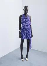 Vestido corto de poliéster, color azul con estampado de lunares blancos. Presenta cuello pico cruzado, tirantes anchos y diseño evasé con cierre lazo cruzado en la cintura.