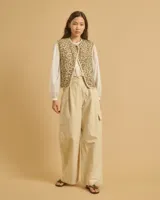 Chaleco corto color beige, con cuello redondo, cierre frontal con un botón y dos bolsillos delanteros.