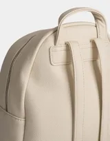 Mochila pequeña de cuerina color rosa pálido, con moño en relieve en el frente y llavero con forma de corazón trenzado. Tiene correas regulables, manija superior, cierre superior, bolsillo frontal con cierre y bolsillos laterales.