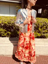 Vestido largo de lino con estampado tie-dye en tonos naranja, rojo y amarillo. Tiene breteles finos y volados en el ruedo.