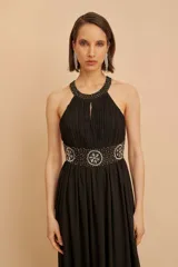 Vestido largo de fiesta negro, con cuello halter, espalda descubierta y falda de gasa. Presenta un aplique de pedrería en la cintura.