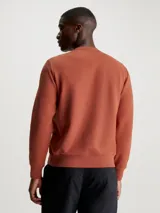Buzo color ladrillo de algodón y poliéster con cuello redondo, puños y bajo acanalados. Presenta un pequeño logo de Calvin Klein en el pecho.