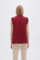 Blusa sin mangas color crudo con cuello con lazo y volados en los hombros.