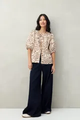 Blusa estampada color beige y blanco, con mangas abullonadas, escote redondo y lazos frontales.