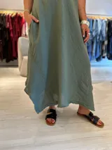 Vestido largo verde musgo de corte acampanado, con mangas cortas, cuello en V y detalle de picos desiguales en el ruedo. Incluye bolsillos laterales.