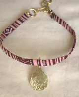 Gargantilla con cinta de tela estampada en tonos marrón y blanco, con dije dorado en forma de gota.