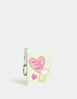 Llavero con dije de libreta de silicona color verde claro, con diseño en relieve de un corazón con la frase "Wake up and do your best", un batido y un corazón pequeño. Incluye cadena metálica con aro.