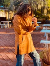 Tapado camel de cuero ovino con cuello clásico, cierre frontal con botones, bolsillos laterales y corte a la rodilla. Diseño slouchy y cómodo.