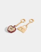Set de dos charms intercambiables dorados con mosquetón. Incluye un dije de cartera con moño y un dije de manzana esmaltada en rojo con strass.