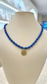 Collar de cuentas facetadas color azul eléctrico con dije circular dorado con incrustaciones de cristales azules.