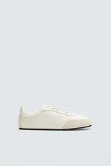 Zapatillas deportivas de cuero color blanco hueso, con puntera de gamuza color crema y suela de goma negra.
