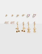 Set de seis pares de aros dorados con diferentes dijes: bolitas, caramelos, corazones rosas, moños blancos, cerezas y ositos.