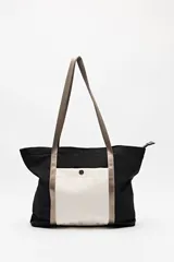 Bolso tote de nylon negro con bolsillo frontal blanco, asas largas de cinta negra y cierre superior.