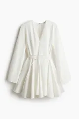 Vestido corto blanco con escote en V profundo, mangas largas con abertura en los puños, cierre oculto en la espalda y cinturón fino extraíble.