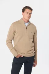 Buzo tejido de lana color beige, con medio cierre metálico y cuello alto. Tiene un pequeño logo bordado en el pecho.