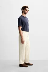 Pantalón color crudo de tejido con textura de rizo, corte relaxed fit, con cintura elástica, bolsillos frontales y traseros, cierre frontal con cremallera y botón.