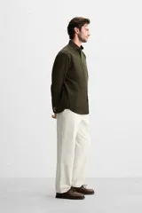 Camisa verde oscuro de corte regular, confeccionada en tejido de mezcla de algodón y lyocell. Tiene cuello italiano, manga larga con puños abotonados y cierre frontal con botones.