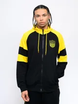 Campera deportiva negra con capucha y detalles en amarillo, cierre frontal y escudo del Club Atlético Peñarol en el pecho. Presenta cortes y cambios de color en mangas y cuerpo, y un estampado en la espalda.