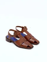 Sandalias de cuero color borgoña con textura croco, diseño cerrado en la parte delantera con aberturas laterales, punta cuadrada y cierre con hebilla ajustable en el tobillo. Taco ancho de 3 cm.