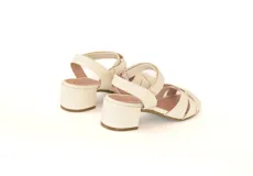 Sandalias de cuero color hueso, con tiras cruzadas en el empeine, talón descubierto y tobillera con hebilla. Taco cuadrado de 4 cm.