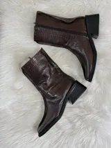 Botas cortas color chocolate con textura de cocodrilo, punta cuadrada y tacón bajo. Cuentan con cierre lateral.