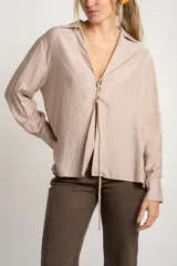 Blusa color visón de viscosa y poliéster con cuello camisero, mangas largas con puños abotonados y cierre frontal con lazos.