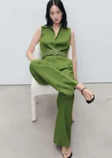 Mono largo color verde oliva, de lino, con corte camisero, cuello clásico, cierre frontal cruzado, sin mangas, cinturón trenzado desmontable y bolsillos laterales.