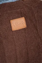 Cardigan de tejido de punto grueso color marrón oscuro, con escote en V y cierre frontal de botones redondos color hueso. Presenta un diseño texturado con líneas verticales marcadas.