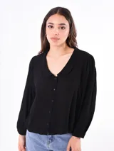 Camisa negra con cuello bebé, manga larga abullonada y cierre frontal con botones.