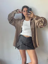 Camisa color dorado de satén con cuello clásico, cierre frontal con botones, mangas largas abullonadas con puños abotonados y corte holgado.