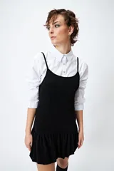 Vestido corto negro de lurex, sin mangas, con breteles finos ajustables y volados en el ruedo.