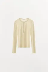 Camiseta color crema de algodón con cuello redondo, manga larga y cierre frontal con botones.