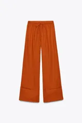 Pantalón palazzo color ladrillo confeccionado en lino 100%, de tiro medio con cintura ajustable con cordones, bolsillos laterales ocultos en costura y pierna ancha.
