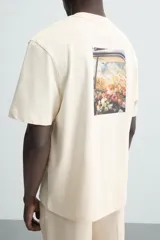 Camiseta color crudo de corte relaxed fit, con cuello redondo y mangas cortas. Presenta un pequeño bordado de flores en el pecho y un estampado fotográfico en la espalda.