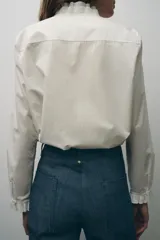Camisa blanca de algodón con cuello con volantes y mangas largas con puños fruncidos.