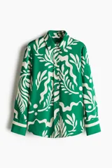 Camisa de manga larga verde con estampado de hojas blancas. Tiene cuello clásico, cierre con botones y puños con botón.