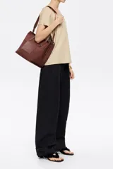 Bolso shopper mediano Bimba y Lola color negro, con doble asa de mano y correa bandolera ajustable y extraíble. Presenta un parche rectangular con el logo de la marca en la parte frontal.