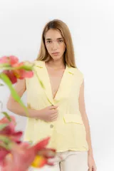 Chaleco amarillo pastel sin mangas, con solapas y cierre con dos botones.
