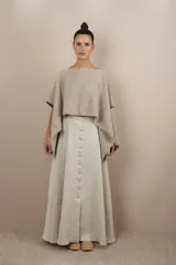 Poncho color beige con diseño a cuadros, cuello bote y terminaciones desflecadas. Tiene aberturas para los brazos en los laterales y detalles en cuero.