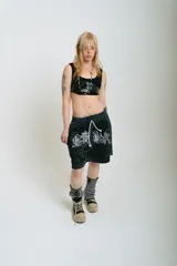 Bermuda de felpa negra con efecto lavado (washed) que aclara hacia los laterales. Presenta un gran estampado serigrafiado en blanco con motivos florales y caracteres orientales estilizados. Posee cordón de ajuste en la cintura y remaches metálicos cromados en los laterales.