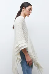 Capa tejida color negro, con cuello redondo, diseño de punto y detalles de lentejuelas. Presenta flecos en el dobladillo.