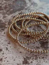 Pulsera elástica compuesta por cuentas redondas pequeñas de 3mm, con acabado dorado.