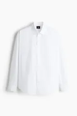 Camisa blanca de popelina de algodón con cuello inglés, tapeta clásica, dos bolsillos superiores abiertos, canesú con pliegue de caja en la espalda, mangas largas con puños abotonados, tapeta de manga con botón y bajo levemente redondeado. Corte holgado.