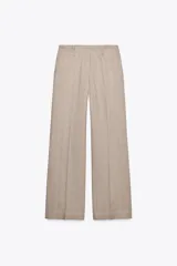 Pantalón de tiro bajo color beige, con bolsillos delanteros y falsos bolsillos de vivo en la espalda. Piernas rectas y cierre frontal con cremallera, botón interior y ganchos.