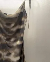 Vestido corto de mesh con estampado abstracto en tonos marrones y negros. Tiene breteles finos, escote drapeado y ruedo asimétrico.