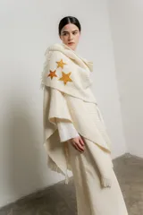 Ruana color crema de tejido grueso con flecos y apliques de estrellas doradas.