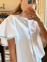 Camisa blanca de mangas cortas con volados y terminación de puntilla celeste.